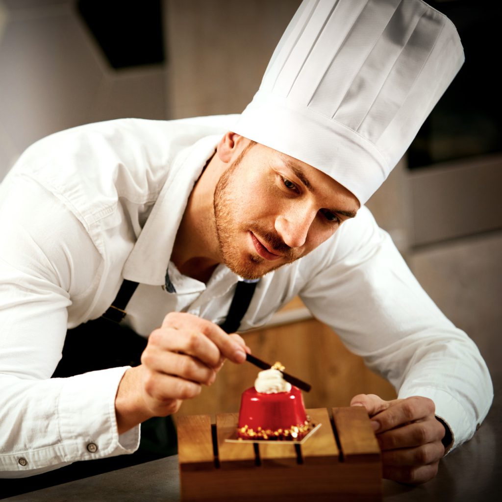 Justin le pâtissier finalise un dessert dans le restaurant où il travaille